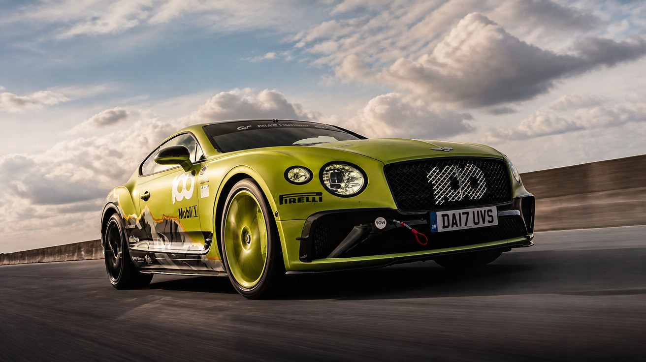 Grüner Bentley Rennsportwagen mit schwarzem Grill und Sponsorenaufklebern fährt auf Asphalt unter bewölktem Himmel.