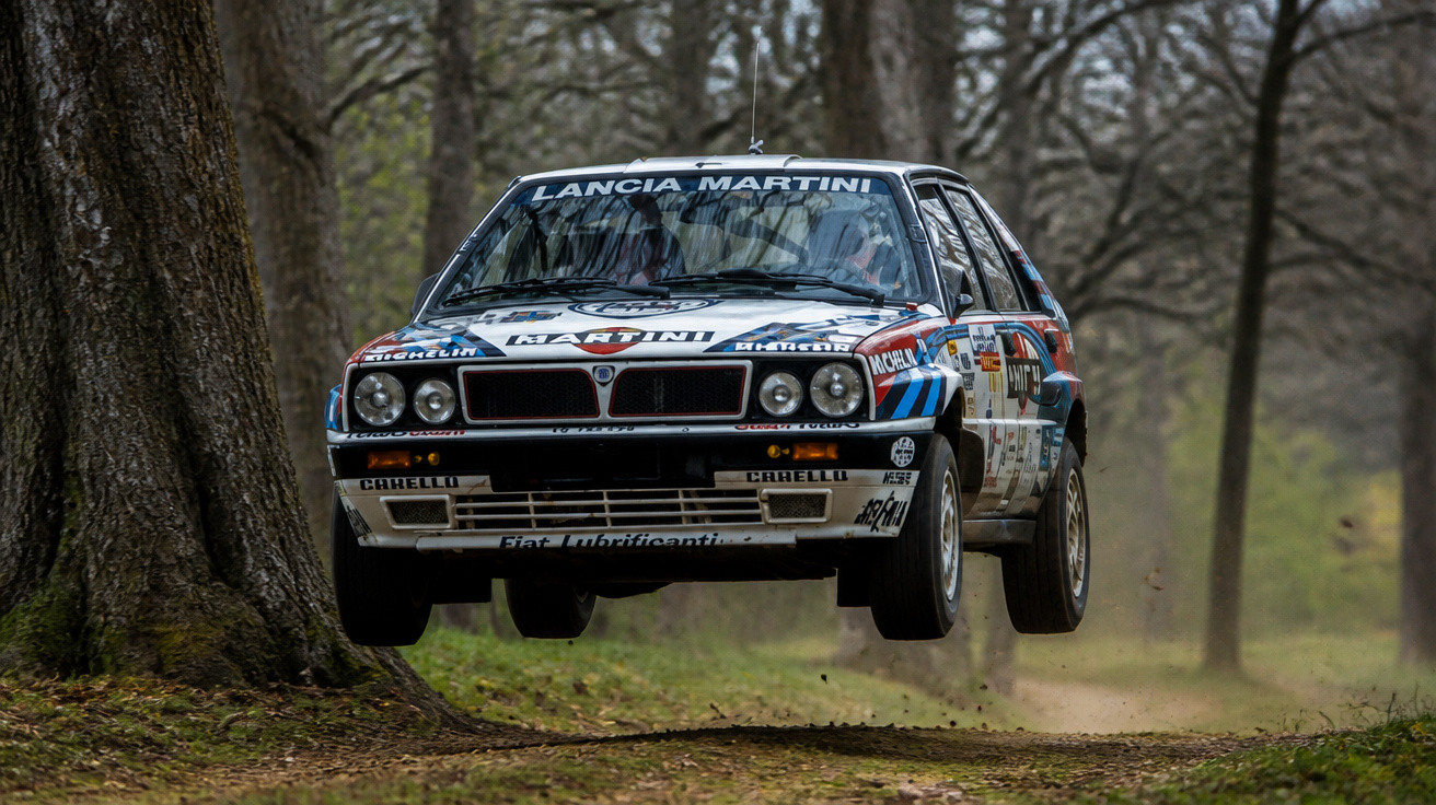 Lancia Martini Rallyeauto springt mit beiden Rädern in einem Waldgebiet über eine Erhebung auf einer Schotterpiste.