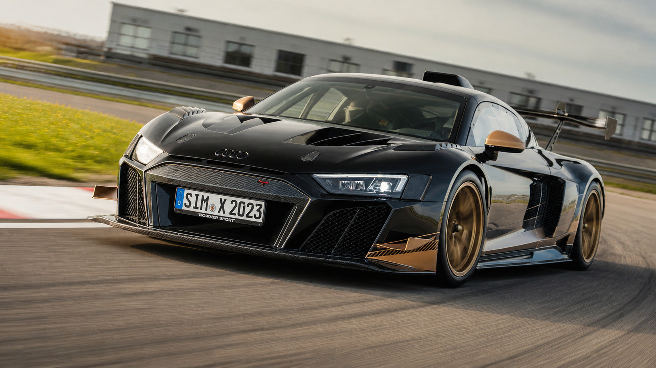 Schwarzer Audi R8 Sportwagen mit goldenen Akzenten fährt auf Rennstrecke bei Tageslicht.