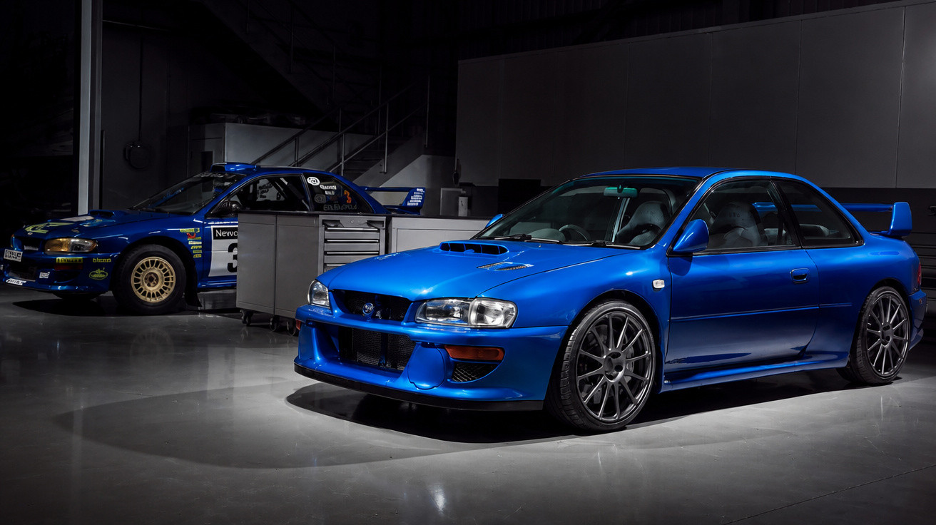 Zwei blaue Subaru Impreza, ein Rennwagen und ein sportlicher Straßenwagen, parken in einer dunklen Garage.