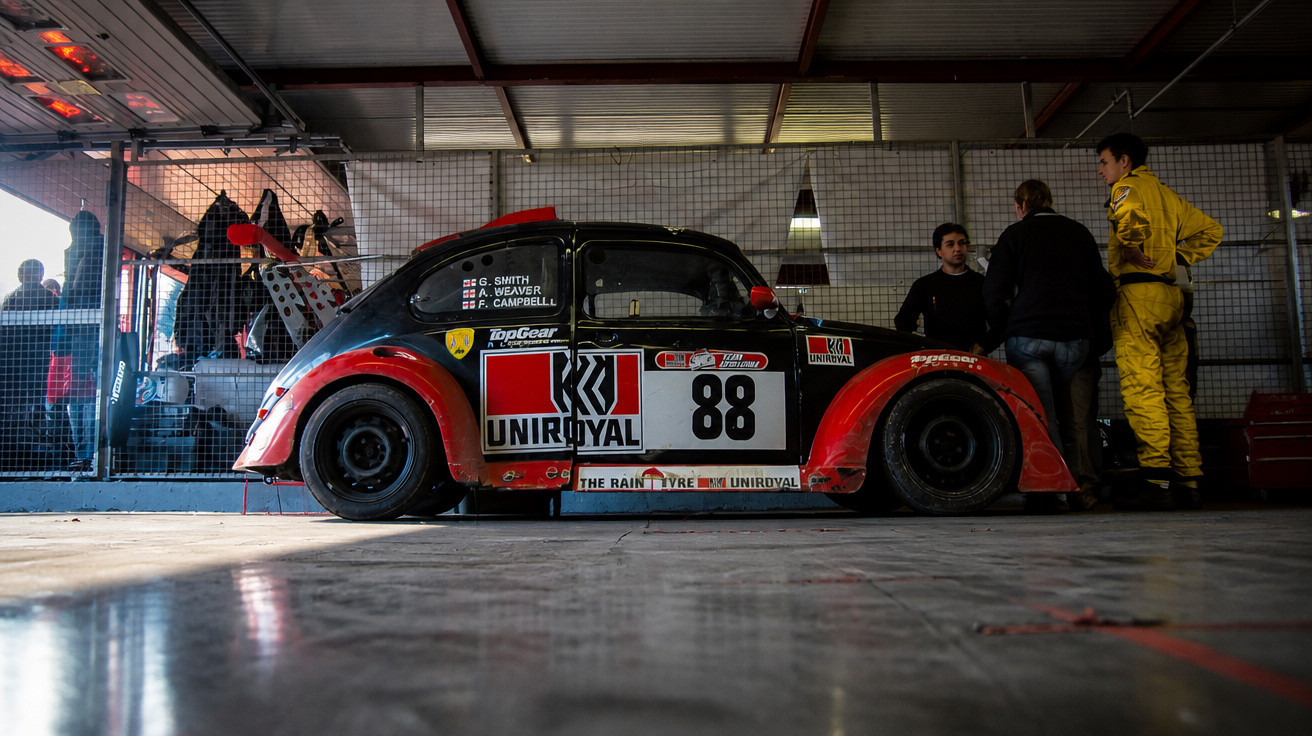 Rennwagen im Retro-Stil mit Nummer 88 und Uniroyal-Logo in einer Garage mit drei Personen.