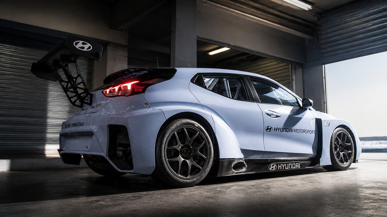 Weißer Hyundai Motorsport Rennwagen mit großem Heckflügel in einer Garage bei Tageslicht.