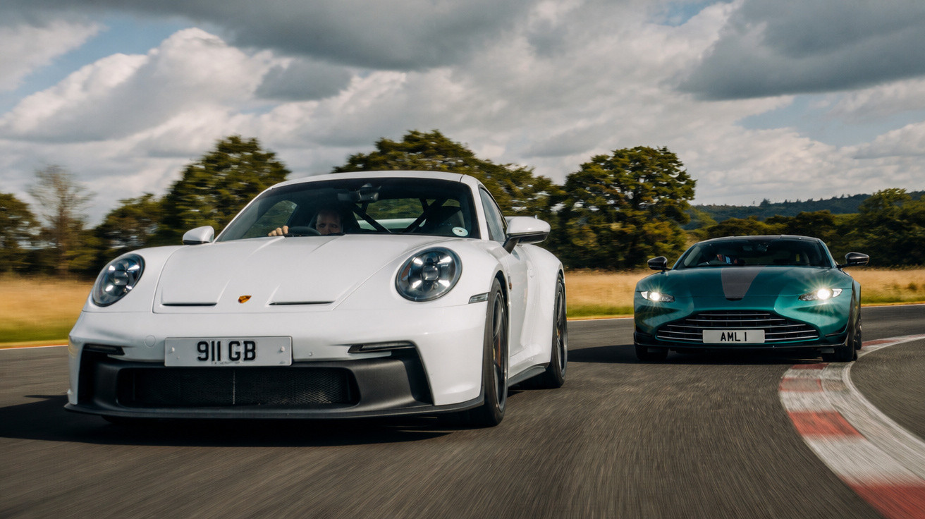 Zwei Sportwagen, ein weißer Porsche 911 und ein grüner Aston Martin, fahren auf einer Rennstrecke.