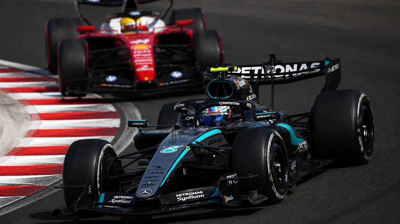 Zwei Formel-1-Rennwagen, vorne Mercedes und dahinter Ferrari, fahren auf einer Rennstrecke in einer Kurve.