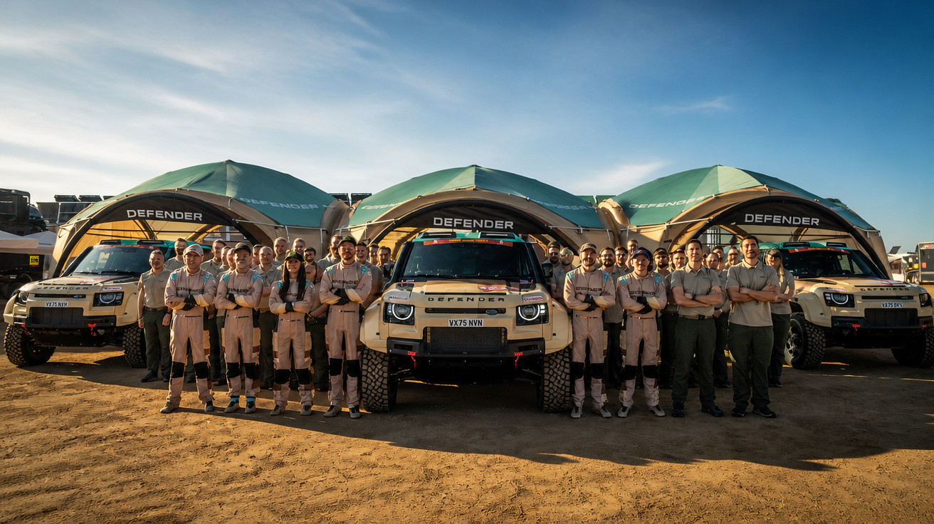 Teammitglieder in Arbeitskleidung stehen vor drei Land Rover Defender Fahrzeugen im Freien bei Tageslicht.