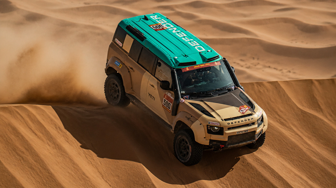 Geländewagen Land Rover Defender fährt schnell durch sandige Dünen in der Wüste bei Renneinsatz.