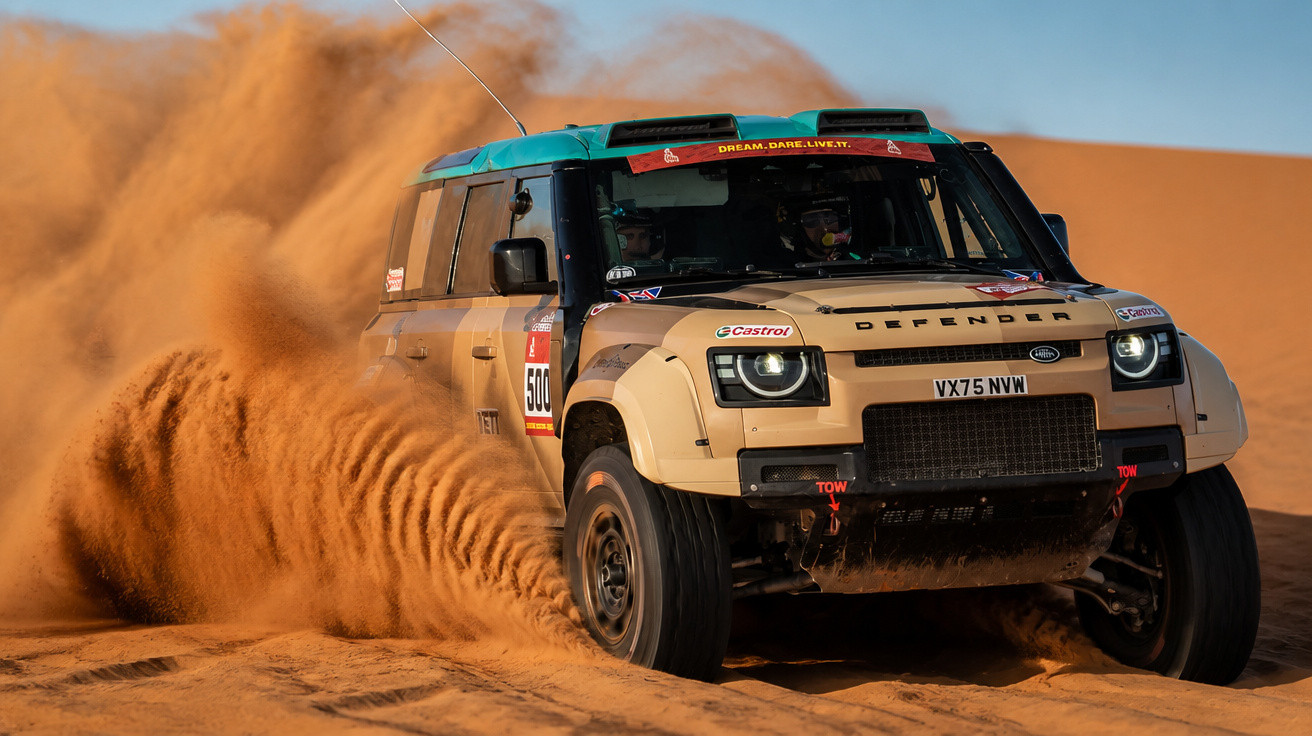 Geländewagen Land Rover Defender fährt schnell durch Sand und wirbelt Staubwolken auf.