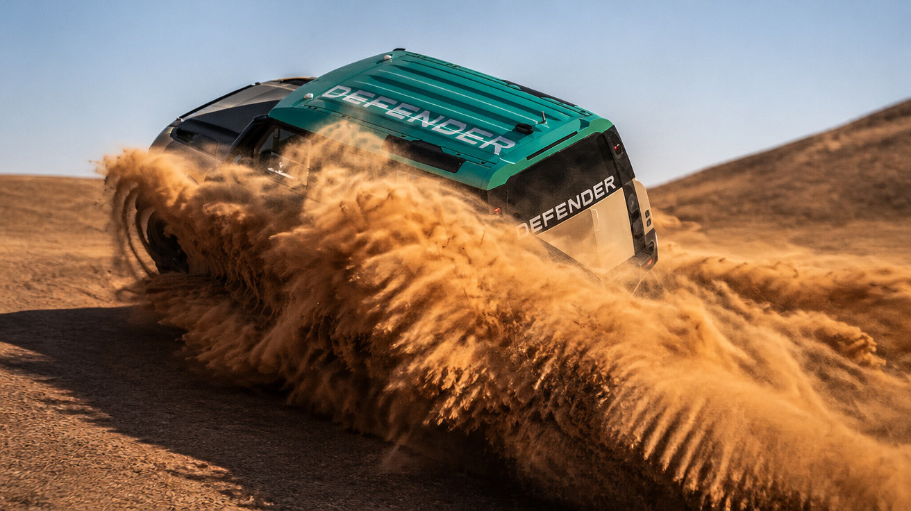 Geländewagen Land Rover Defender fährt durch staubige Wüstenlandschaft und wirbelt Sand auf.